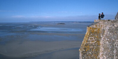 Mont Saint-Michel (F). The monastery was built in the early eighth century on a rock in the shallow Saint-Malo Bay in the border area between Normandy and Brittany. The bay has the highest tidal variations in France with a 10-12-metre difference between high and low tide. Twice a day, tidal waves flood the bay and surround the monastery. Today the island is connected to the mainland by a two-kilometre causeway.